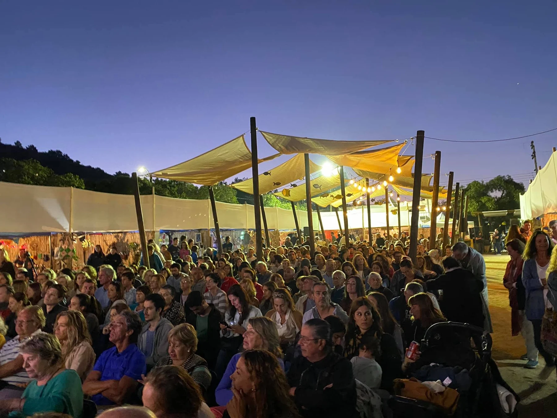 Público asistente en una actividad al aire libre bajo cubiertas textiles de sombra